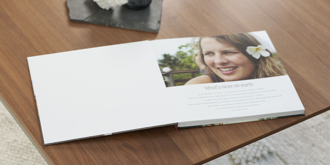 On a wooden table lies an open photo book with an introductory text and a photo of Lea Wippermann with a flower in her hair. Above the photo book is a dark tray with a candle and shell.