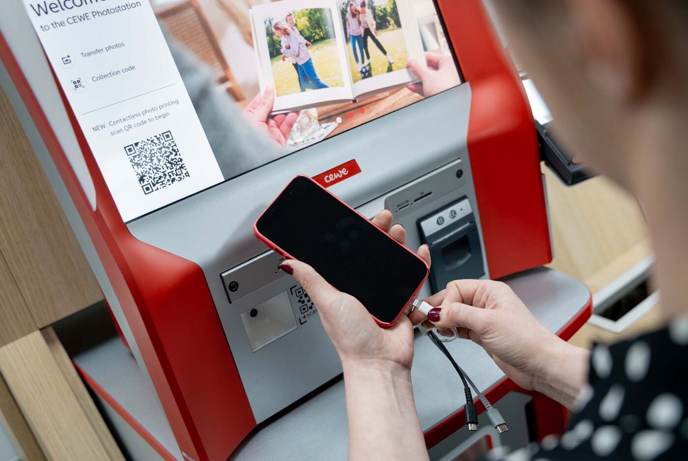 Person connects their smartphone to a CEWE terminal to order a photo book.