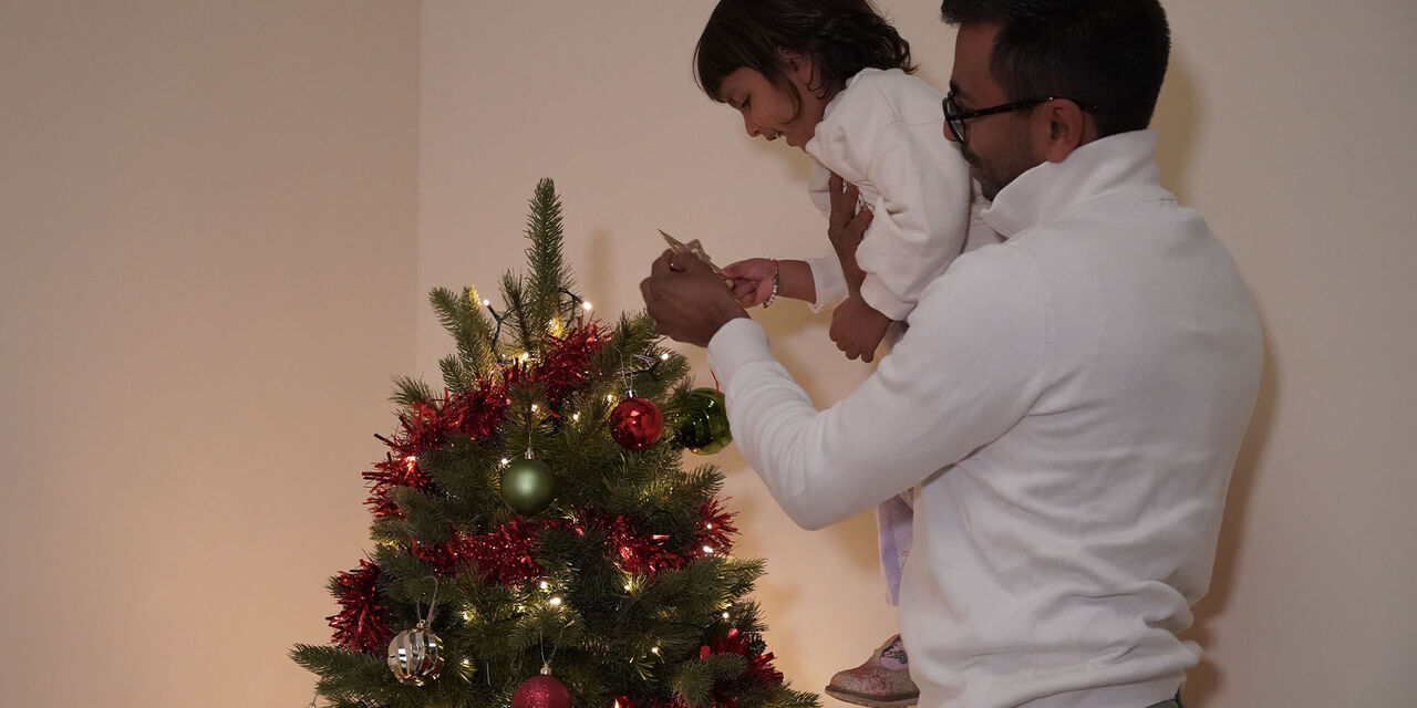 Father holding daughter up in the air to place the star on the Christmas tree.