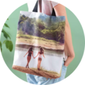Two friends hold hands at the beach, carrying a personalized CEWE photo bag with their shared picture.