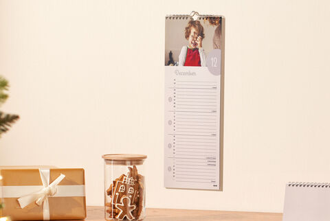 A beautiful wall calendar with a child in a red dress in December. Next to it is a glass with gingerbread figures and a gift box with a bow.